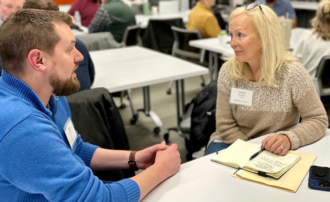 A man and a woman sit at a table and talk during a workshop.
