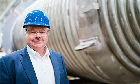 Enerfab CEO Scott Anderson stands in front of a large metal tank wearing a hard hat and safety goggles