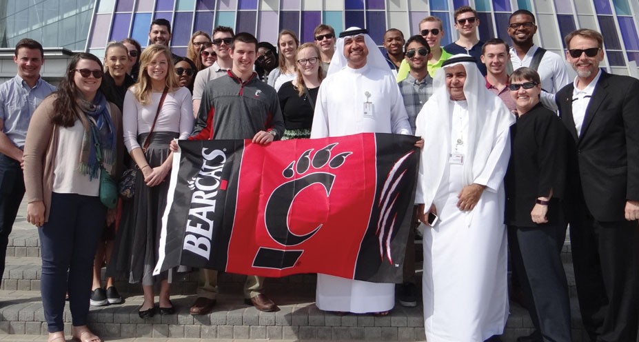Lindner students and faculty pose with their hosts in Dubai, holding a Bearcats flag
