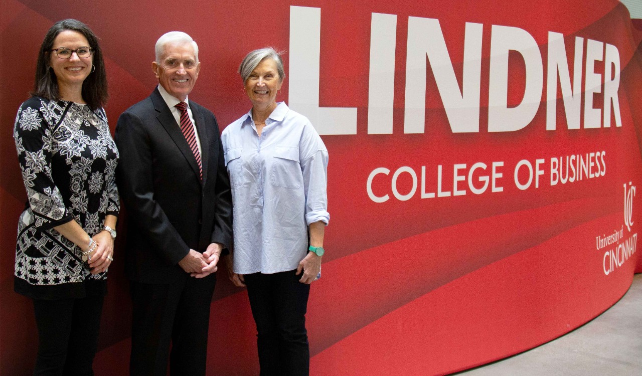 Two women and one man in professional dress stand in front of a red Lindner banner.