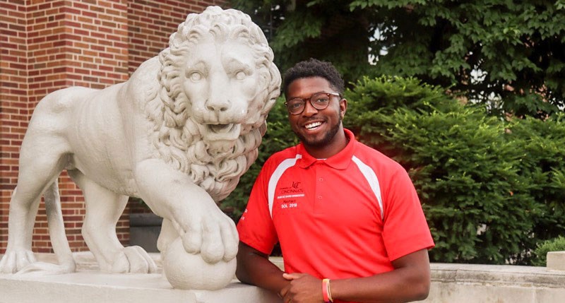 Nonso Okonji poses with one of the lion statues in front of McMicken Hall