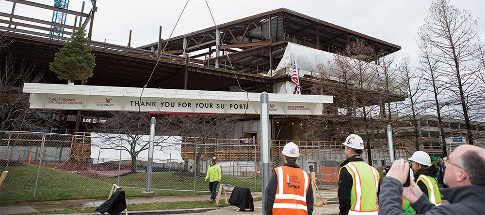 The final steel beam for the new Lindner College of Business building being lowered, with construction personnel in the foreground