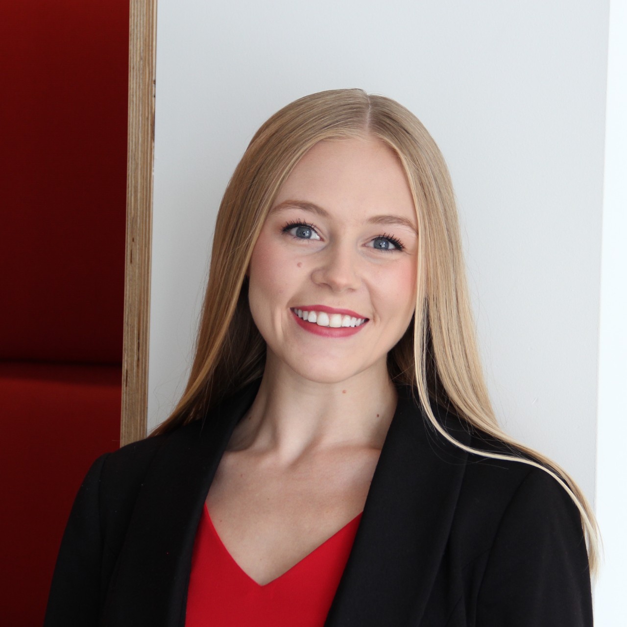 Headshot of Anna Schulte wearing red blouse and black blazer in front of white wall