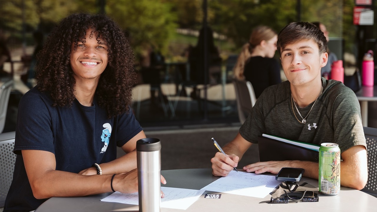 Two students study together at a table outside Lindner Hall.