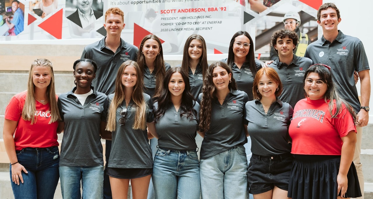 Lindner students in gray shirts and red shirts pose for a group picture in the Lindner atrium.